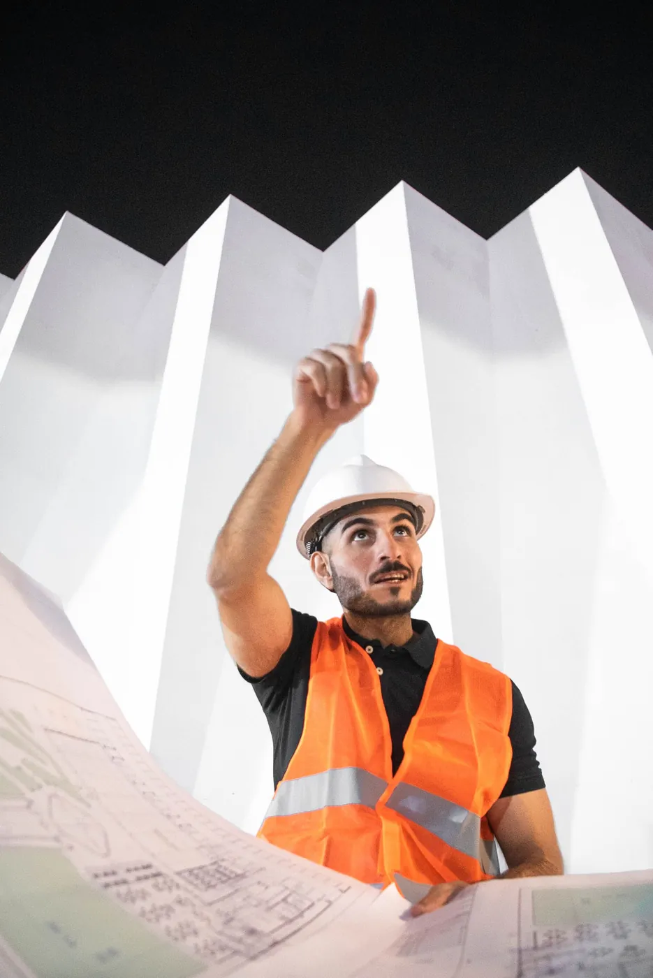 Ingénieur en casque et gilet orange consultant des plans de chantier