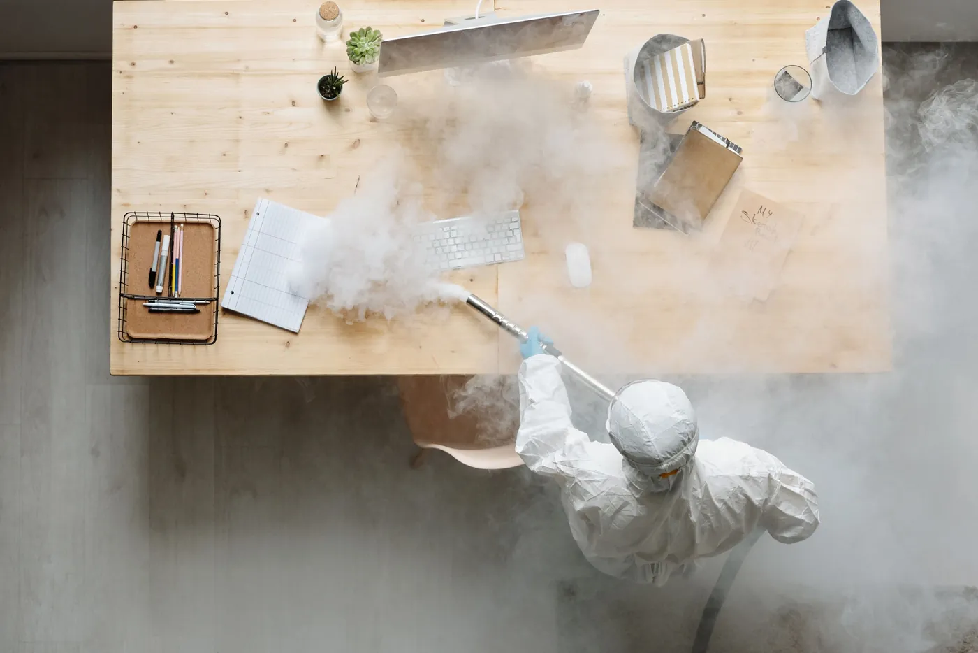 Désinfection d'un bureau par un technicien en combinaison blanche, vue du dessus